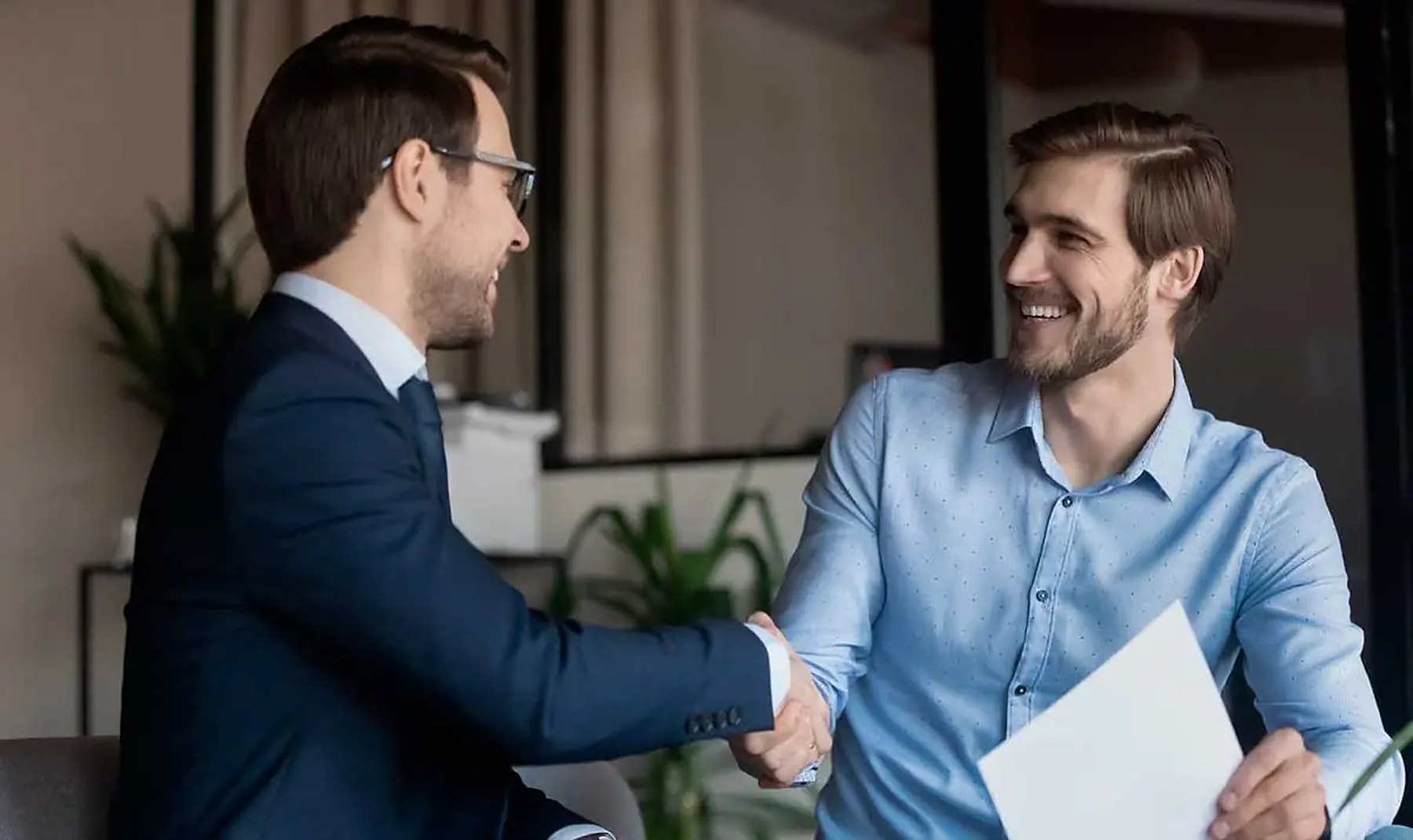 Dos personas dándose la mano y sonriendo en una reunión de trabajo